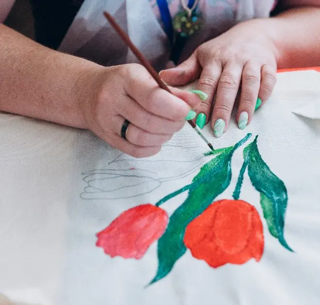 A woman paints a colorful flower design on a white tablecloth