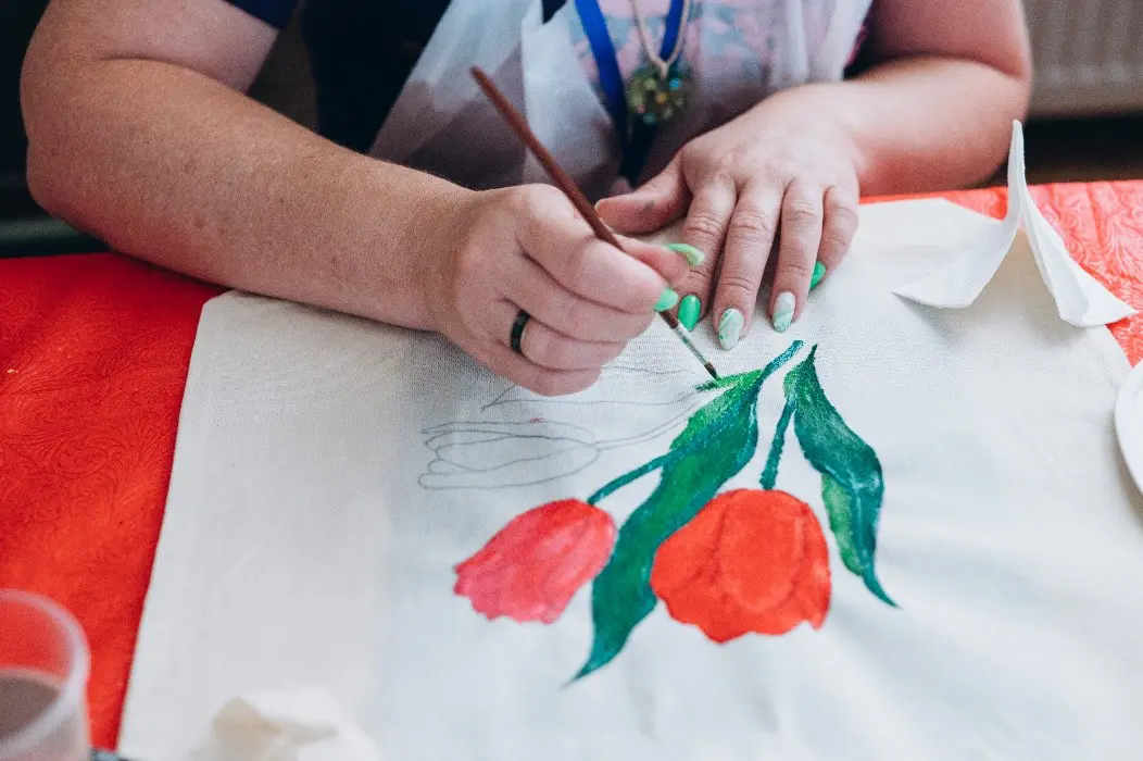 A woman paints a colorful flower design on a white tablecloth